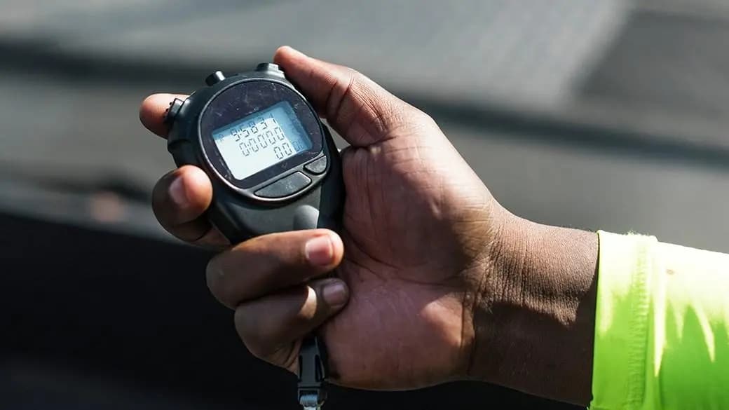 Mão segurando um cronômetro digital durante a cronometragem de uma prova esportiva